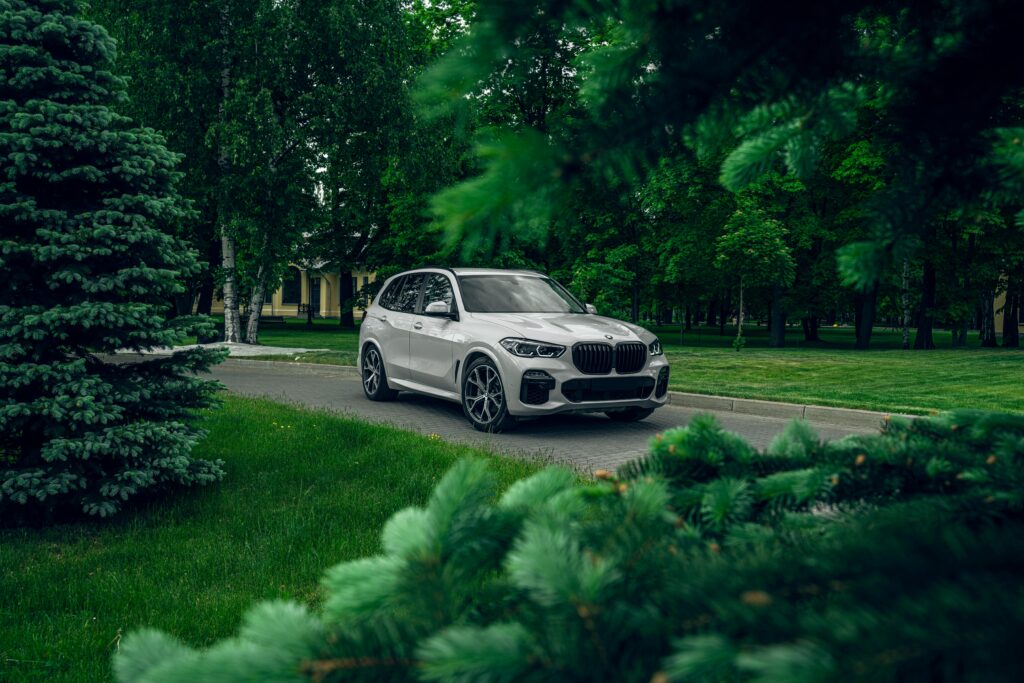 A sleek white SUV parked amidst lush green foliage, capturing a serene park environment.