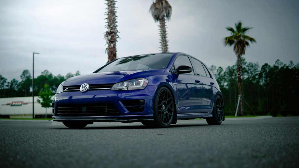 Blue Volkswagen Golf R parked under palm trees, showcasing sleek design and modern style.