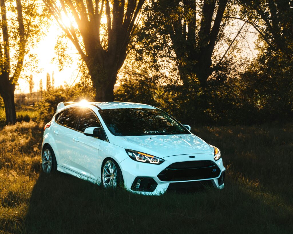 White Ford Focus RS parked in a grassy area with sunlit trees in the background.