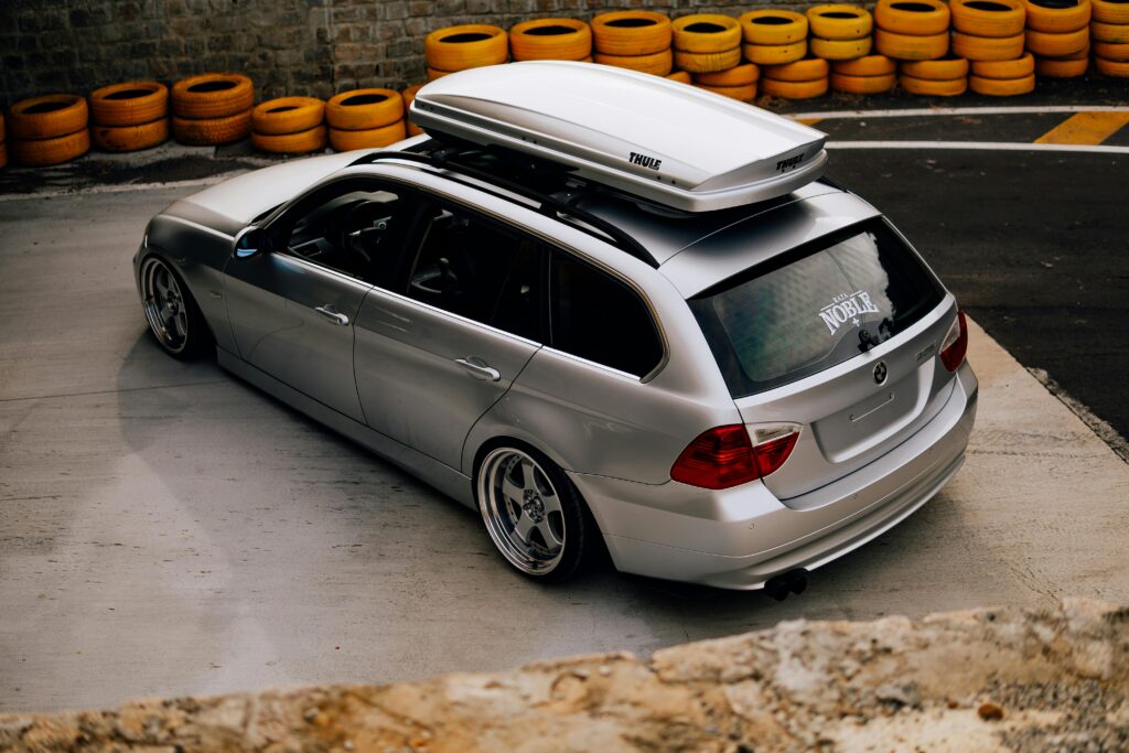 Sleek silver BMW wagon with a roof box at a car meet in Brazil, featuring stanced wheels.